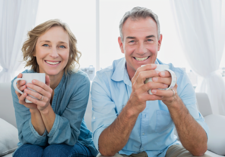 Happy couple holding coffee mugs smiling at camera