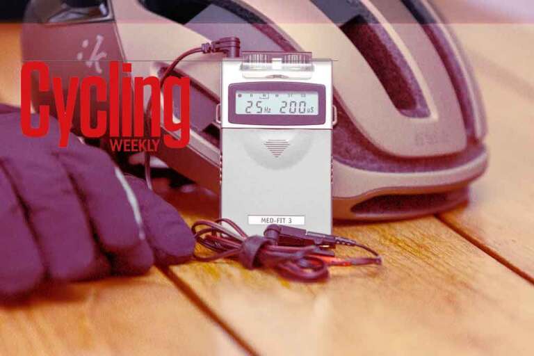 TENS unit displaying 25 Hz next to a cycling helmet and gloves with Cycling Weekly branding