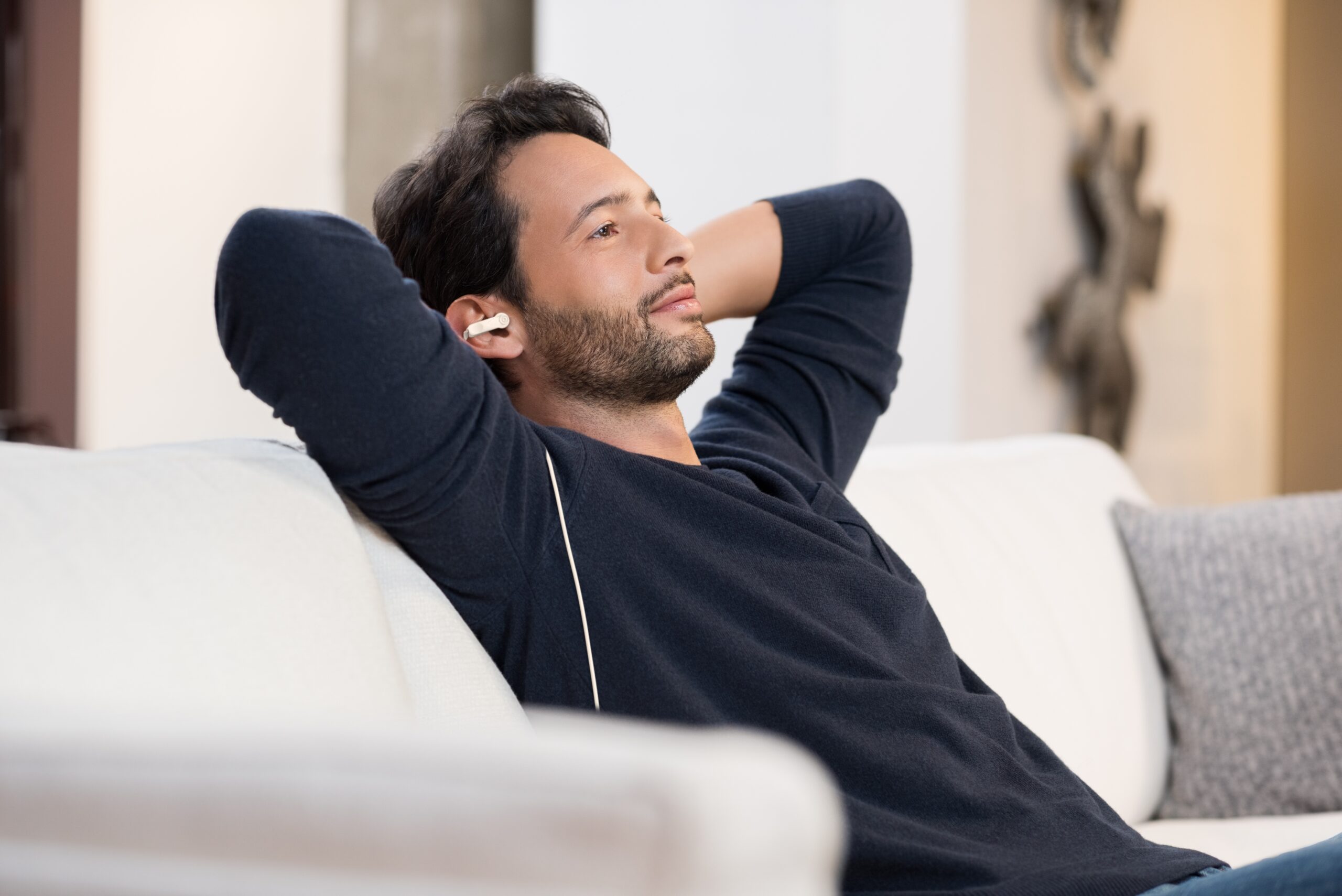 Man relaxing on a sofa with his hands behind his head, wearing the Vagal Buddy ear clip