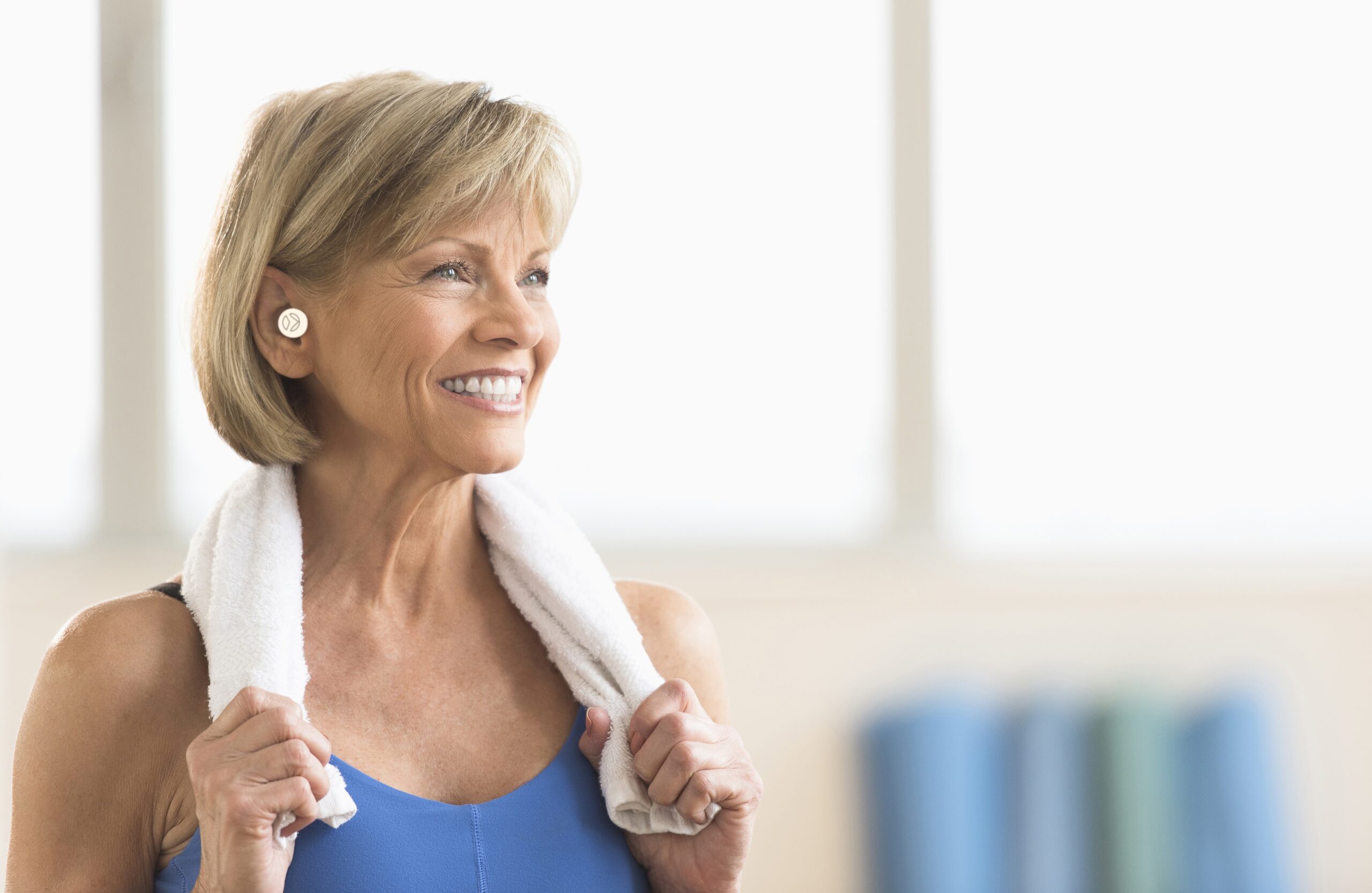 Smiling woman with a towel over her shoulders after a workout, wearing Vagal Oh! on her ear